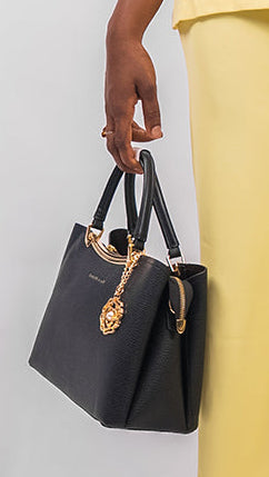 Woman in a yellow outfit holding a black handbag against a white background